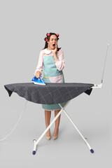 Sticker - Portrait of tired young housewife in apron with iron and ironing board on grey background