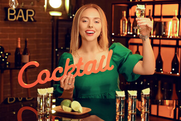 Wall Mural - Young woman with tequila shot and word COCKTAIL in bar at night