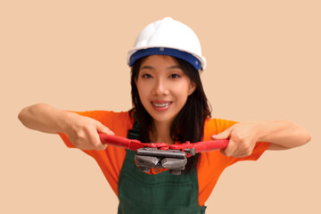 Wall Mural - Asian woman in jumpsuit and hardhat with bolt cutter on beige background