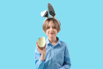 Wall Mural - Cute little boy in bunny ears with chocolate egg on blue background. Easter celebration