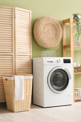 Wall Mural - Modern washing machine with basket, shelving unit and dressing screen near green wall. Interior of home laundry room