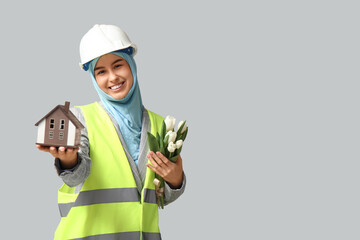 Sticker - Muslim female construction worker with toy house and tulips on white background. Women's Day celebration