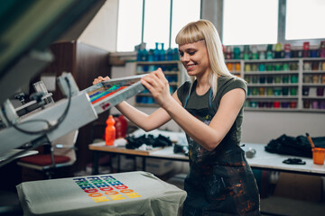 Wall Mural - Smiling print shop worker silkscreen printing on t-shirt at facility.