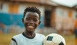 © anatoliycherkas - African American boy in black and white football uniform smiling and holding ball in stadium