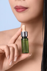 Poster - Beautiful woman with bottle of hair oil on blue background, closeup