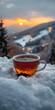 A coffee cup sits in the snow with a sunset in the background