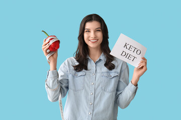 Wall Mural - Happy smiling young woman holding paper sheet with text KETO DIET, bell pepper and measuring tape on blue background