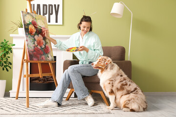 Wall Mural - Pretty young woman painting with cute Australian Shepherd dog at home