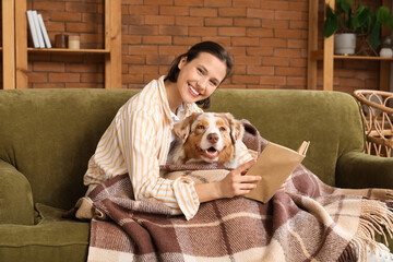 Poster - Pretty young woman reading book with cute Australian Shepherd dog on sofa at home