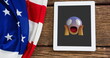 A tablet displaying shocked emoji rests on a wooden surface beside American flag