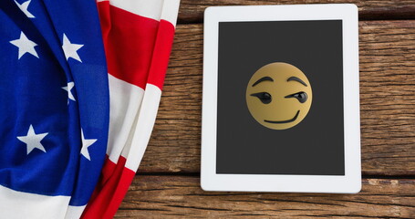 Wall Mural - A tablet displaying winking emoji rests beside American flag