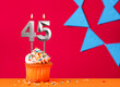 Birthday cupcake with candle number 45 on a red background with blue pennants