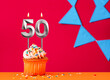 Number 50 candle with birthday cupcake on a red background with blue pennants