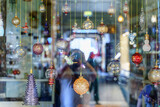 Fototapeta Do pokoju - A close-up view of a glass storefront behind which glass multicolored holiday balls hang on a string, with reflection, blurred, in Souq Waqif bazaar, Doha, Qatar