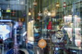 Fototapeta Do pokoju - A close-up view of a glass storefront behind which glass multicolored holiday balls hang on a string, with reflection, blurred, in Souq Waqif bazaar, Doha, Qatar
