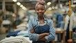 A cheerful African American seamstress with her arms casually crossed strikes a confident pose in a bustling clothing factory gazing directly at the camera