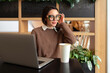 Woman Wearing Glasses using Laptop. Charming businesswoman in eyeglasses and casual clothes working with laptop computer while siting cafe. Elegant female adjusting her glasses looking side