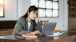 © Satori Studio - Woman seated at a cafe table, expressing concern while looking at her laptop screen, with hand on forehead.
