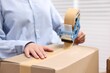 © New Africa - Parcel packing. Post office worker taping box indoors, closeup