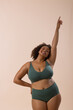 © Wavebreak Media - A biracial young female plus size model with curly hair is posing confidently on a beige background,
