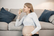 Pregnant lady sitting near a sofa in living room holding an apple