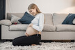 Pregnant lady sitting near a sofa in living room and touching her belly