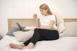 Pregnant lady lie on a bed and holding an apple while using a laptop