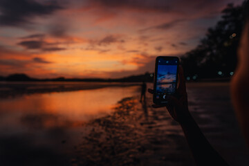 Wall Mural - Smartphone takes photos of the calm beach and sky at In the evening at Ao Nang, Krabi.