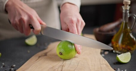 Canvas Print - Woman slicing lime fruit in a half on a wooden cutting board at domestic kitchen