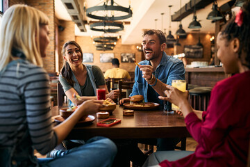 Cheerful friends having fun while talking and eating in pub.