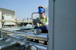 © ultramansk - Young technician with hard hat and safety vest adjusts equipment on a commercial building's rooftop amidst an urban landscape under a clear sky.