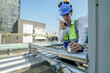 Service engineer in protective gear working on heating and cooling systems atop a city building, surrounded by metallic ductwork under the midday sun