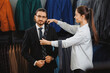 Young beautiful female consultant offering accessory tie to handsome businessman in menswear store. Boutique shop of classic clothes for business men