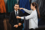 Fototapeta  - Young beautiful female consultant offering accessory tie to handsome businessman in menswear store. Boutique shop of classic clothes for business men