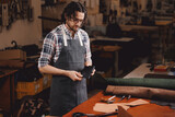 Fototapeta  - Portrait happy tailor working with natural brown leather in workshop. Small business of shoemaker cobbler