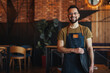 Portrait of Owner / Waiter at Restaurant. Portrait of handsome young male coffee shop owner standing at cafe. Portrait of a handsome barista in t-shirt and apron