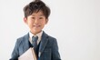 白い背景の幸せな表情をした若い日本人男の子が本とペンを持っています - 放課後のプログラム、教育の卓越性、学習後の勉強