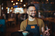 Waiter carrying tray with cappuccino cups in a cafe. Close up of handsome barista holding two cups of coffee in the cafe. Young waiter serving coffee in a cafe and looking at camera.
