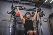 A strong and fit Asian man engages in hanging knee raises at a gym, targeting his core and abs for a toned physique.