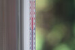 Outdoor thermometer behind the glass on a green blurred background