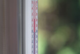 Fototapeta Tulipany - Outdoor thermometer behind the glass on a green blurred background
