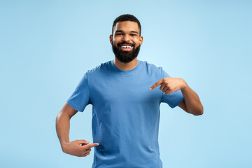 Wall Mural - Portrait of smiling African American man pointing with fingers at copy space over blue background