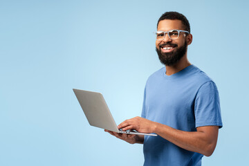 Wall Mural - Smiling African American man in eyeglasses typing on the laptop while looking at camera