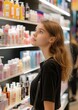 © LoLArt - Vertical photo of young thoughtful customer woman or girl standing in a cosmetics store choosing goods for her skincare and hair care for beauty sphere products advertising campaign