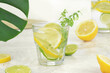Lemonade with lemon and green leaves decorated with citrus fruits on marble table; monstera leaf. Summer time.