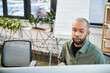 © Bliss - A disabled african american man with myasthenia gravis immersed in work, sitting at a desk in front of a computer screen in a busy office setting
