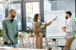 © Bliss - Diverse group standing in front of whiteboard, collaborating on project ideas in a modern office setting.