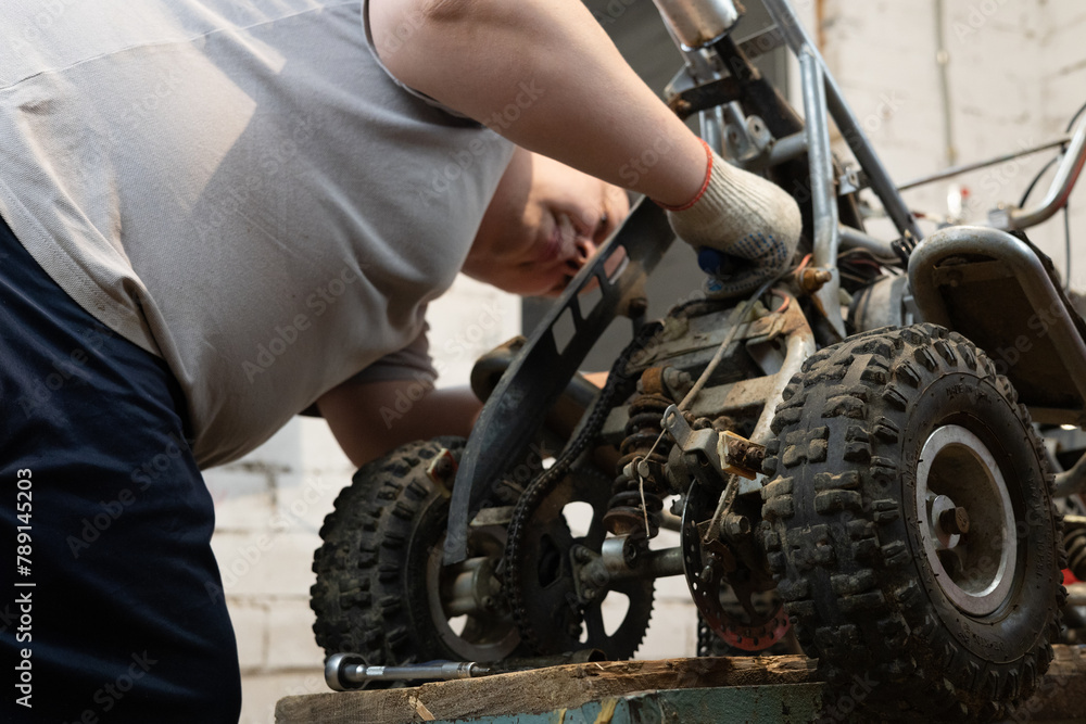 Installing a new part on an ATV to replace a broken old one. Do-it-yourself repair of a children's ATV in the garage for a child. A father is repairing his son's ATV in the garage.