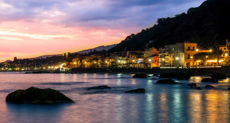 Wall Mural - evening or night landscape of evening town coastline in golden lights and sea gulf with calm water and nice reflections with beautisul sunset sky on background