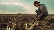 A woman is squatting in a dry field and digging in the ground. A lean year, a drought. She looks at the ground, checks the soil and crops